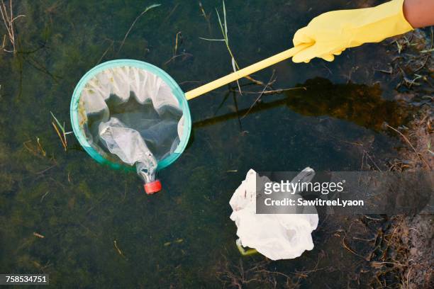 Cropped Hand Removing Bottle From Net Floating In Lake