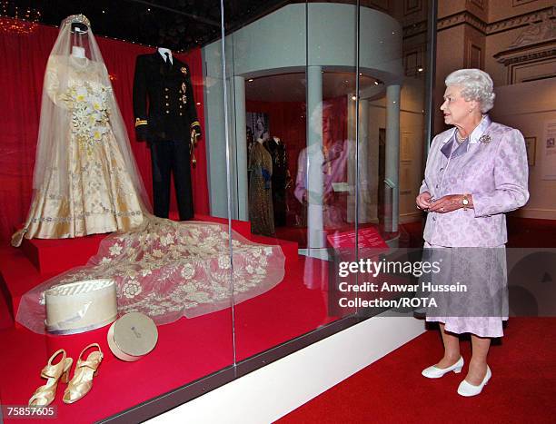 Queen Elizabeth looks at her 1947 wedding gown and 13 foot bridal trail designed by Norman Hartnell with the naval uniform worn by Prince Philip,...