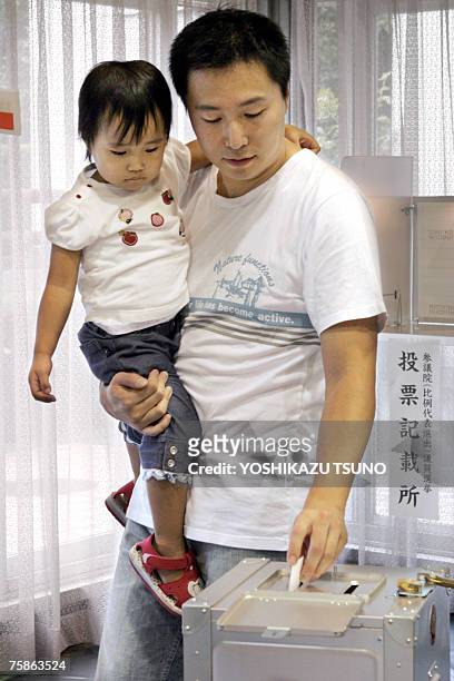 Man, holding his daughter in his arm, casts a vote for the upper house election at a polling station in Tokyo 29 July 2007. Japan voted in an...