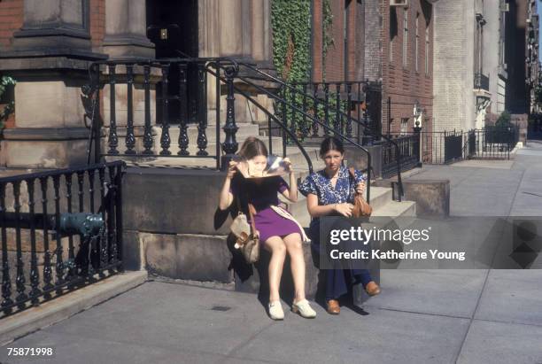 Portrait of two girls as they sit on the stoop of a house on 70th Street, New York, New York, 1970s. One holds a sun reflector under her chin.