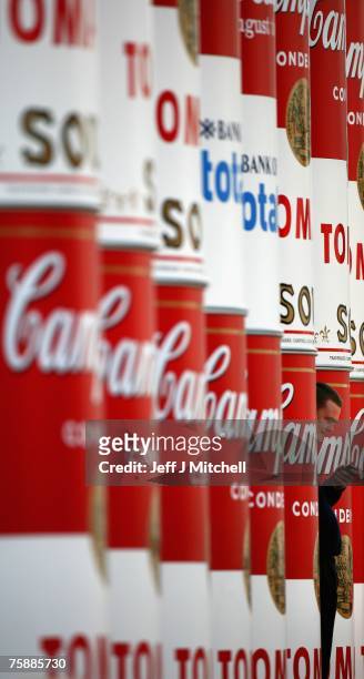 Man uses a mobile phone as he stands between enlarged Campbell's soup cans that are wrapped around the columns of the National Gallery of Scotland to...