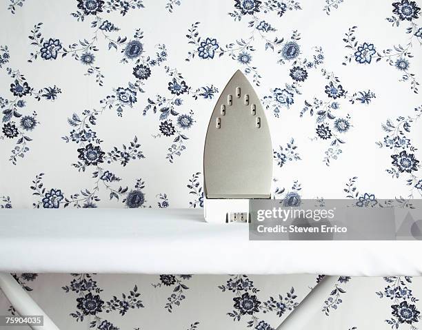 iron on ironing board with wallpaper pattern in background - iron appliance stock pictures, royalty-free photos & images