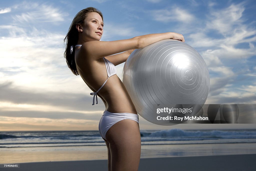Young woman holding large exercise ball on beach