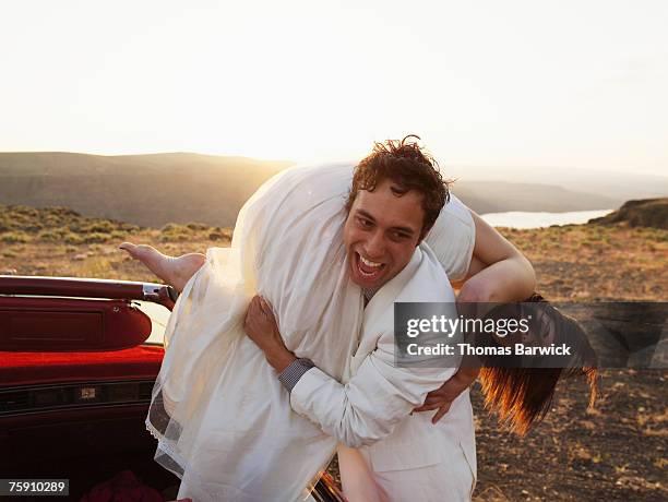 groom carrying bride over shoulder, laughing - bride and groom wedding car stock pictures, royalty-free photos & images