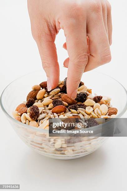 young woman picking at a bowl of nuts - raisin stock-fotos und bilder