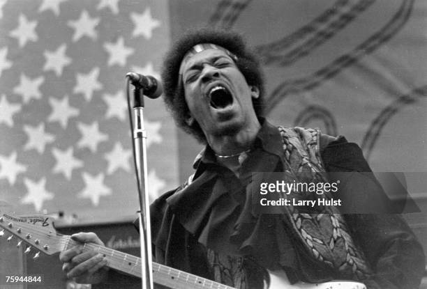 Rock guitarist Jimi Hendrix performs onstage with his Fender Stratocaster electric guitar in front of an American Flag on APRIL 26, 1970 in...