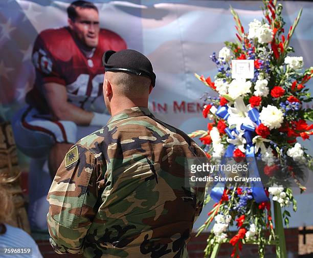 Member of the United States Armed Forces walks past a wreath and poster of Pat Tillman entering the memorial services for the ex-NFL player and Army...