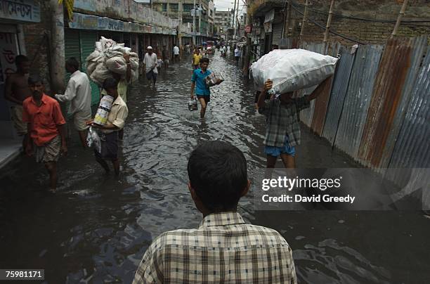 People make their way through a flooded commercial street on August 6, 2007 on the outskirts of Dhaka in Keranigonj, Bangladesh. While water levels...