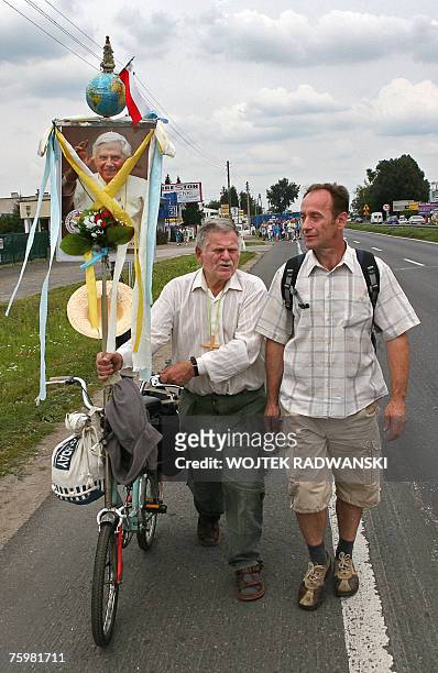Two men walk with a portrait of Pope Benedict XVI attached to a bicycle and are followed by a group of pilgrims from Warsaw through a Warsaw suburb...