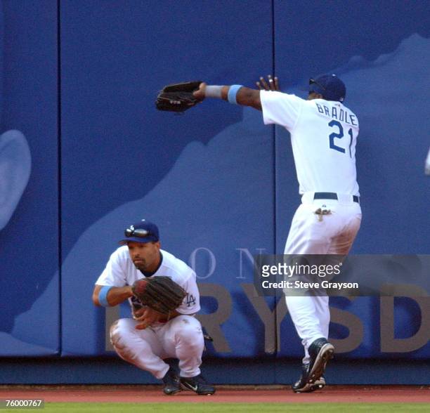 Milton Bradley of the Los Angeles Dodgers hits the wall for a catch as Dave Roberts ducks to avoid a collision during their contest against the New...