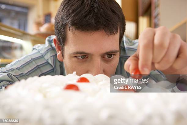 young man putting cherry on top of cake, close-up - cherry on the cake stock pictures, royalty-free photos & images