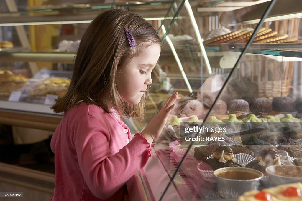 Young girl (9-11) looking at cakes in display cabinets, side view