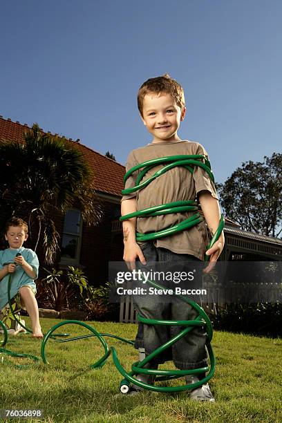 two boys (6-7, 8-9)  playing with water hose in garden - amarrado fotografías e imágenes de stock