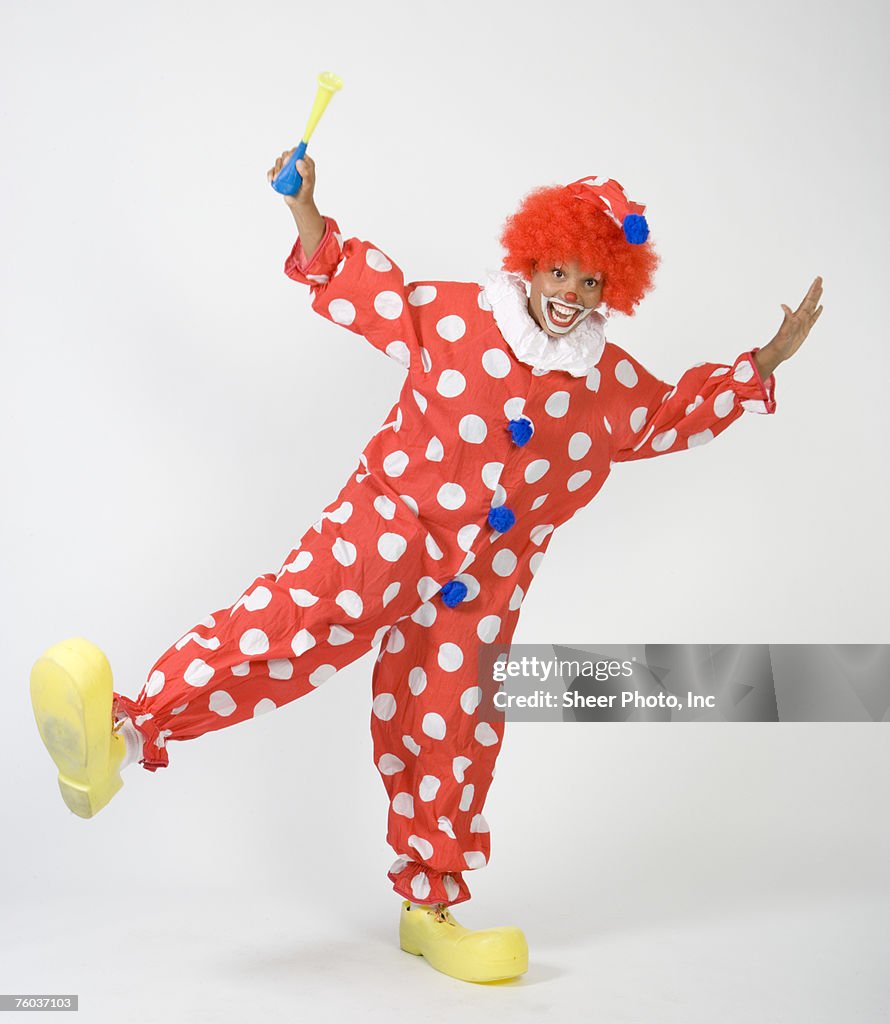 Clown holding horn, standing on one leg, portrait