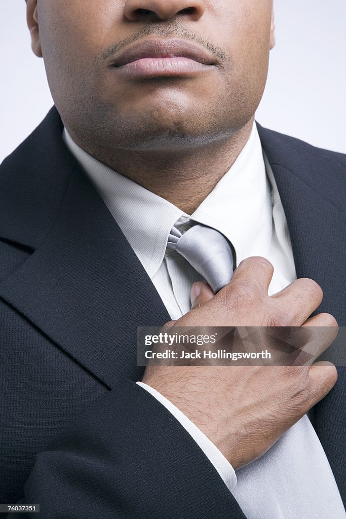Mid adult businessman adjusting tie, mid section