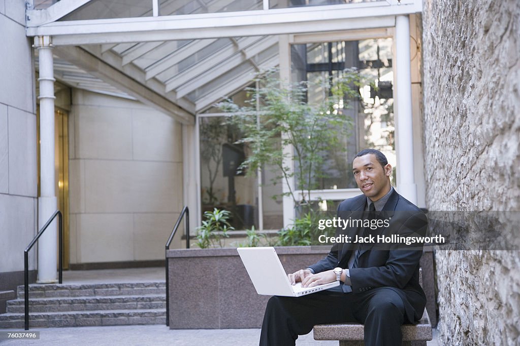 Businessman sitting outside office building using laptop