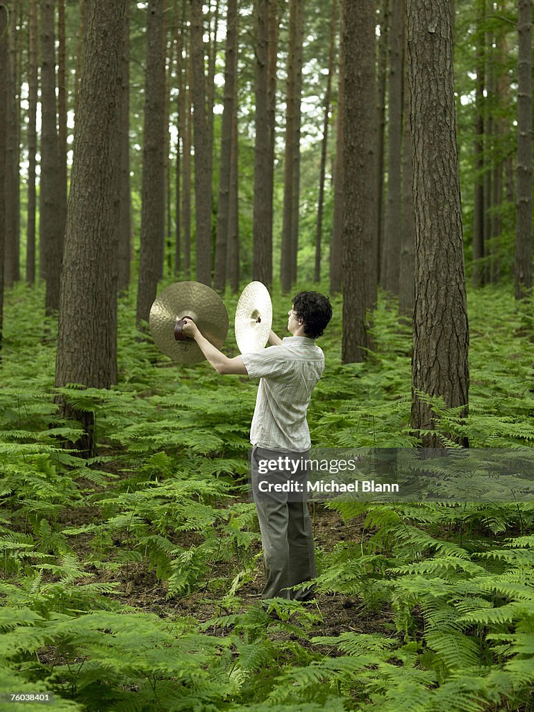 Man playing cymbals in forest, rear view