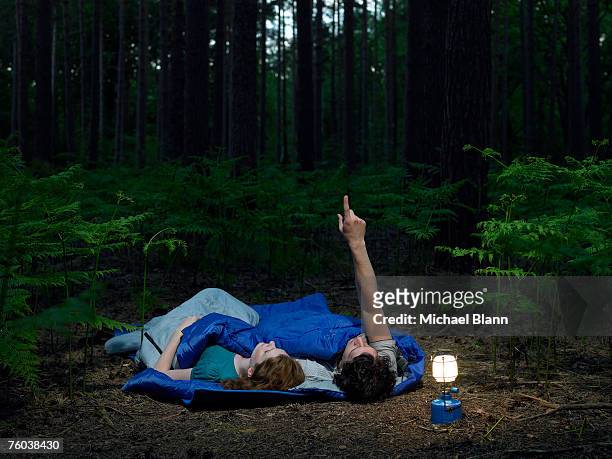 couple lying in sleeping bags in forest with illuminated lantern, man pointing upwards - index finger stock pictures, royalty-free photos & images
