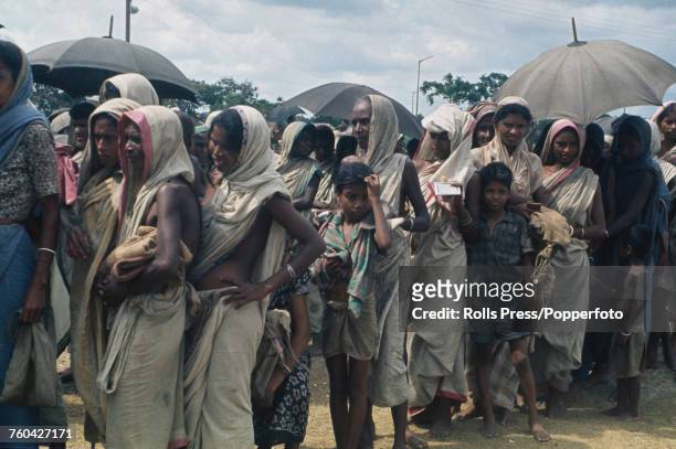 View of a line of women and children lining up together as they shelter from monsoon rain in a refugee camp in East Pakistan during the Bangladesh...