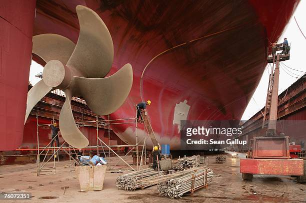 Workers finish maintenance work on a cargo ship's propeller as other workers paint its hull during repairs of the ship at the Blohm & Voss shipyard...