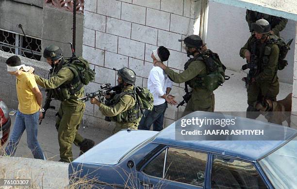 Two hand cuffed and blind folded Palestinian men are marched away after being arrested duing a military raid into the northern Israeli occupied West...