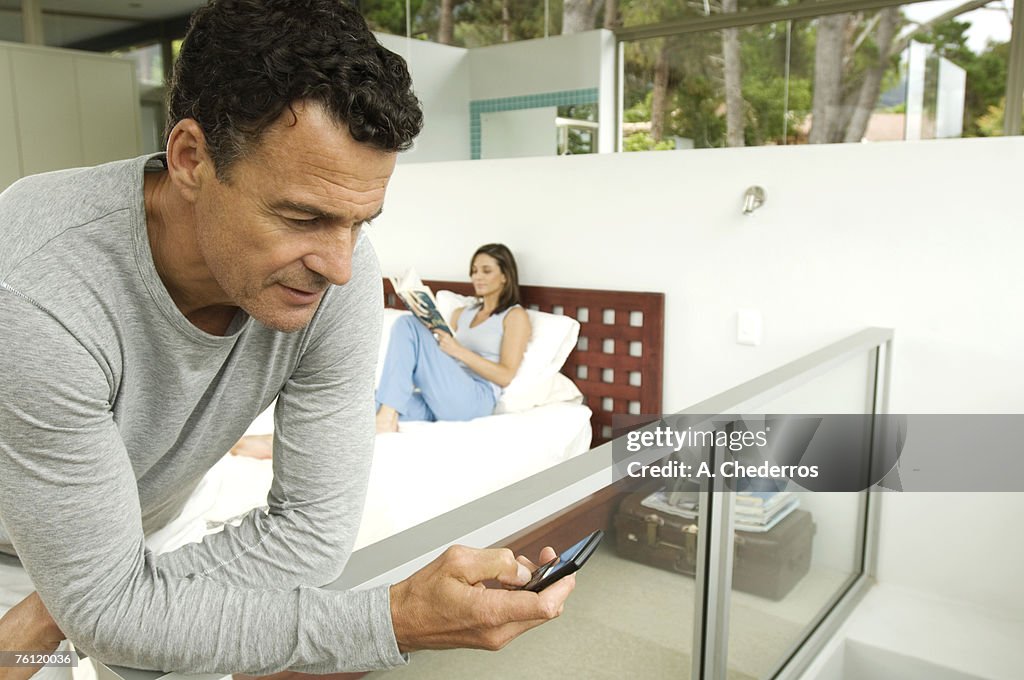 Couple in bedroom, man looking his cell, woman reading magazine, indoors