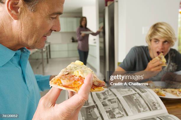 father and teenager eating pizza, mother in background, indoors - teenagers eating with mum stock pictures, royalty-free photos & images