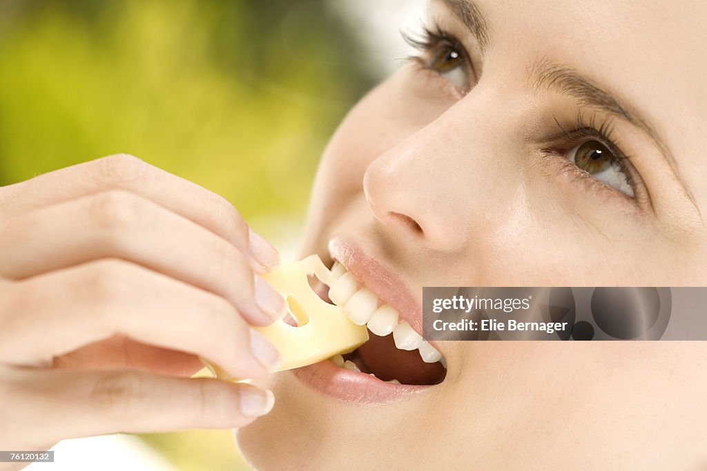 Portrait of a young woman eating a piece of gruyere cheese, outdoors