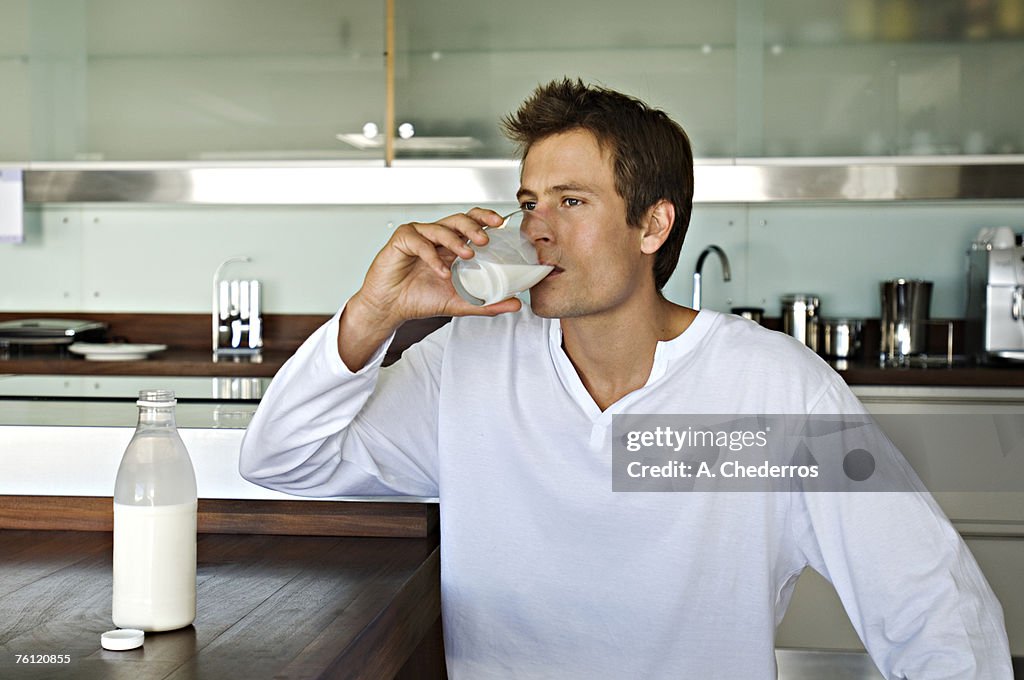 Young man drinking milk in kitchen