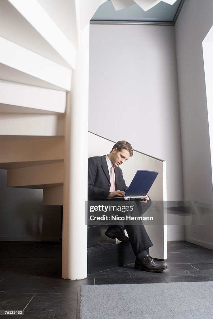 Businessman in staircase using a laptop