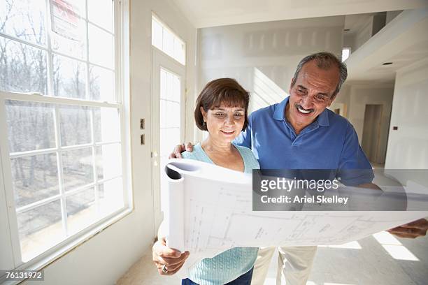 senior hispanic couple looking at blueprints in new house - retirement plan imagens e fotografias de stock