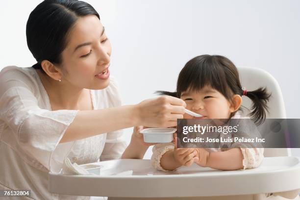 asian mother feeding baby daughter - spoon feeding stockfoto's en -beelden