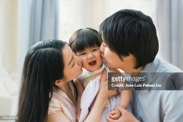 asian parents kissing baby daughter's cheeks - asian mom kid kiss stock-fotos und bilder