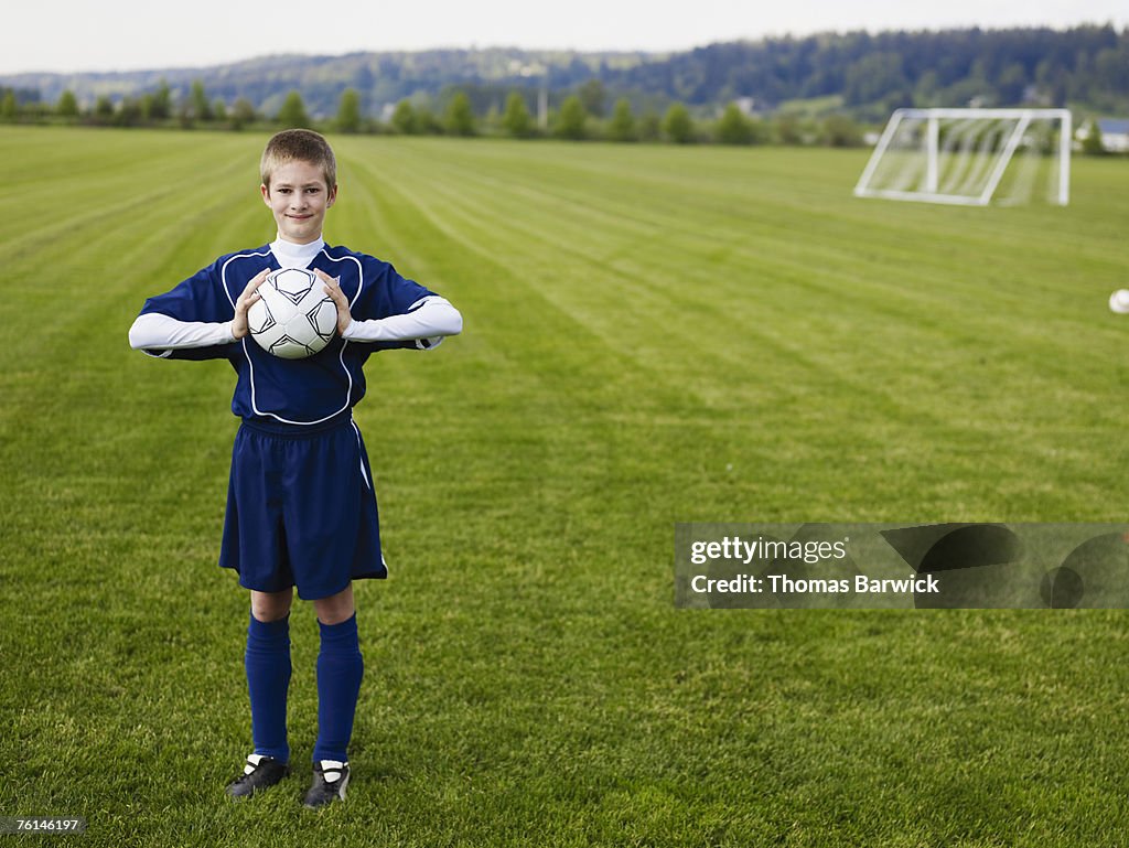 Boy (12-13) standing, holding football, on pitch