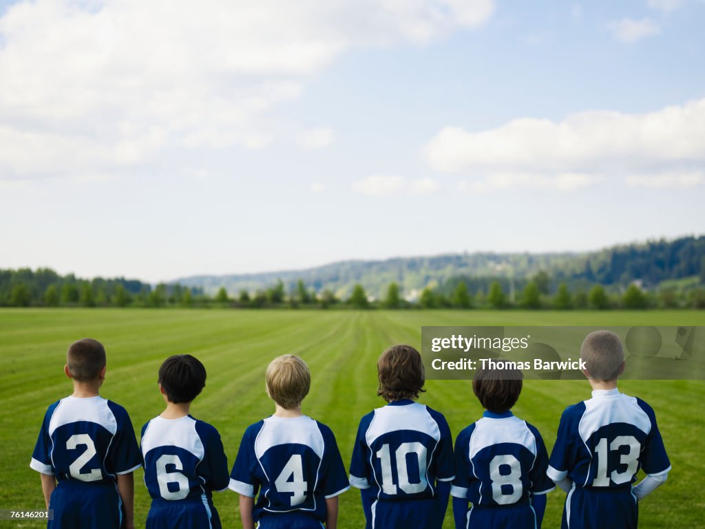 Boys (10-11, 12-13) standing in row in field, rear view, elevated view