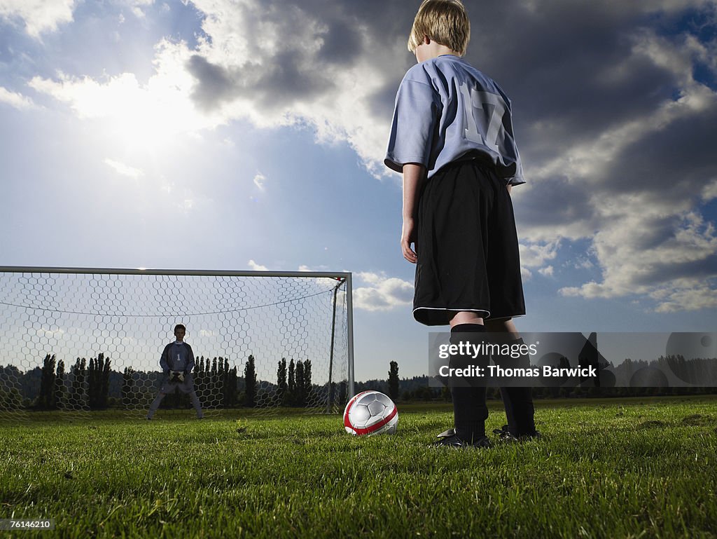 Boys (10-11, 12-13) playing football on pitch, rear view, low angle