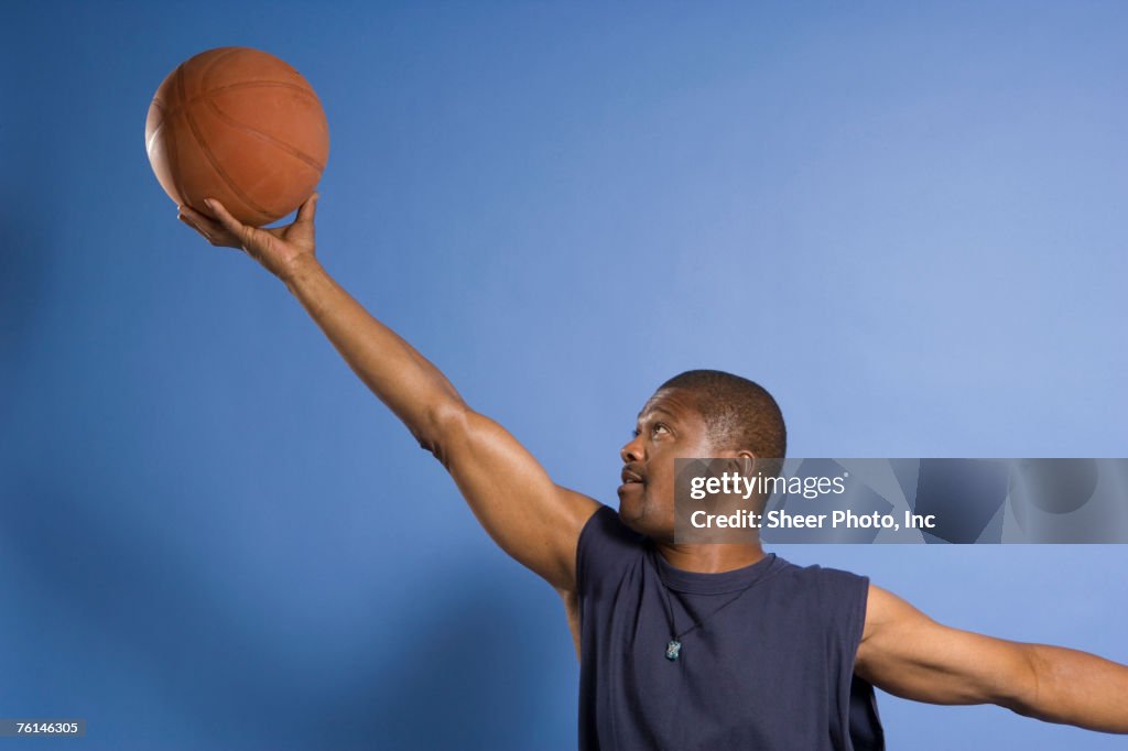 Man doing lay-up with basketball, against blue background, side view