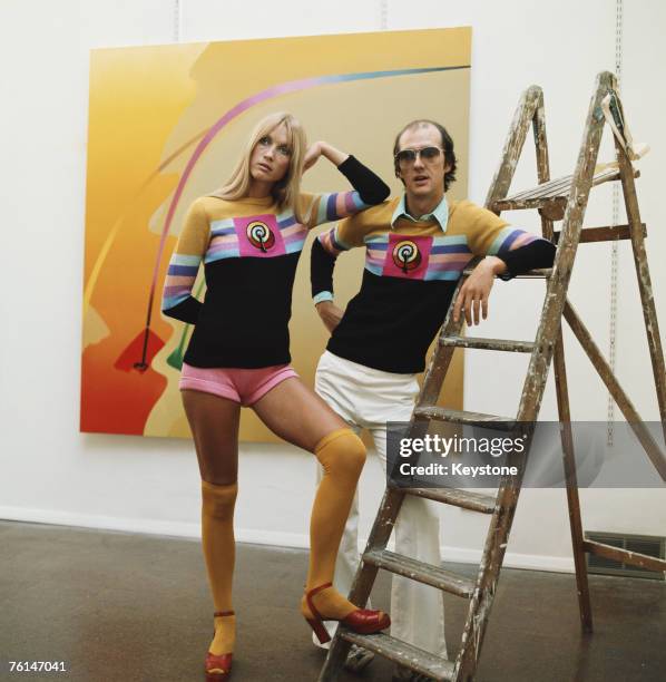 English sculptor and pop artist Allen Jones with a model in a gallery showing his work, circa 1970. The couple are wearing sweaters designed by Jones...