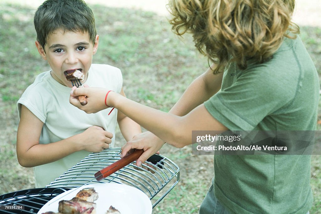 Boy feeding bite of grilled meat to younger boy