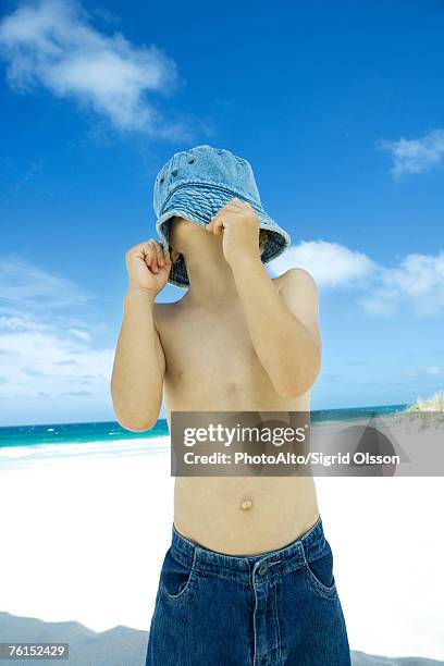 boy pulling hat down over face on beach - bucket hat stock pictures, royalty-free photos & images