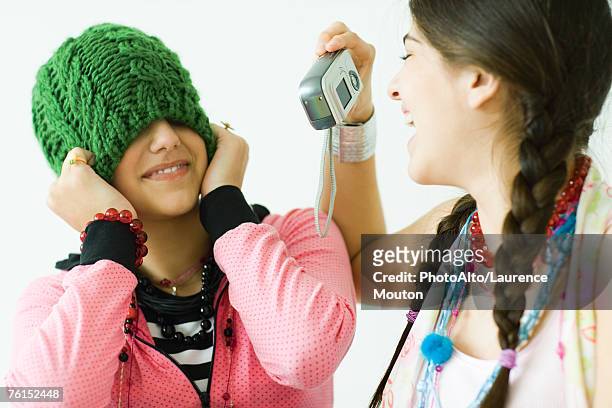 "two young female friends, one taking photo of the other while she pulls hat over eyes" - no confidence stock pictures, royalty-free photos & images