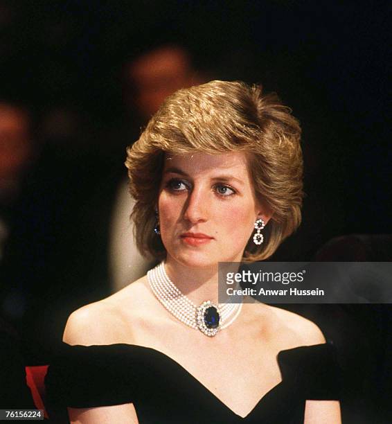 Diana, Princess of Wales, wearing a midnight blue velvet, off the shoulder evening dress designed by Victor Edelstein, a sapphire, diamond and pearl...