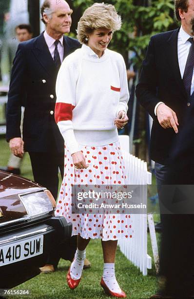 Diana, Princess of Wales, wearing a red and white polka dot skirt designed by Mondi with matching socks, a white jumper and red shoes, attends a polo...