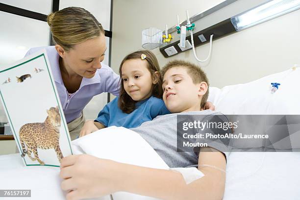 "boy in hospital bed, reading book with mother and sister" - sibling hospital stock pictures, royalty-free photos & images