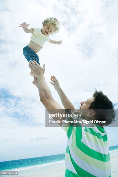 man throwing child into air on beach - 飛行機のまね ストックフォトと画像