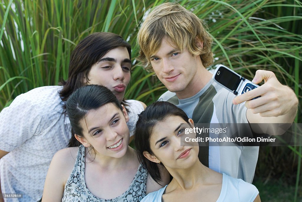 Group of young friends posing while man takes photo with cell phone