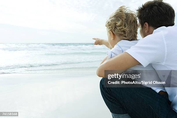 "man looking at ocean with son, rear view" - op schoot stockfoto's en -beelden