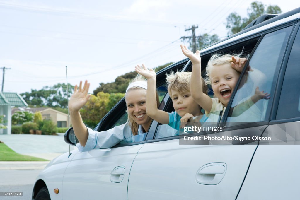 "Mother and two children waving out of car windows, looking at camera"