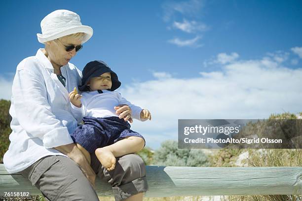"senior woman sitting on wooden railing, holding baby, dunes in background" - blue white summer hat background stock pictures, royalty-free photos & images