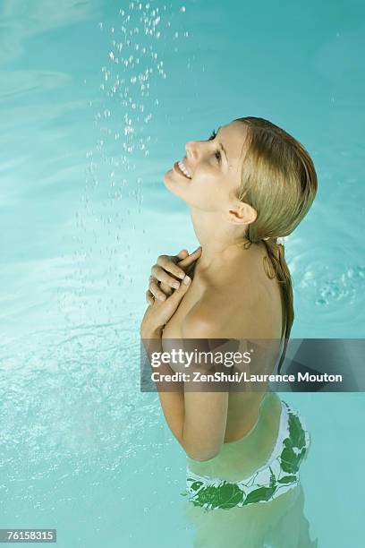 young woman in pool, standing under stream of water, covering bare chest - bare bottom women stockfoto's en -beelden